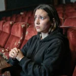 Jeune femme au cinéma regardant un film d'horreur avec une expression de suspense et d'angoisse dans une salle vintage aux sièges en velours rouge