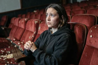 Jeune femme au cinéma regardant un film d'horreur avec une expression de suspense et d'angoisse dans une salle vintage aux sièges en velours rouge
